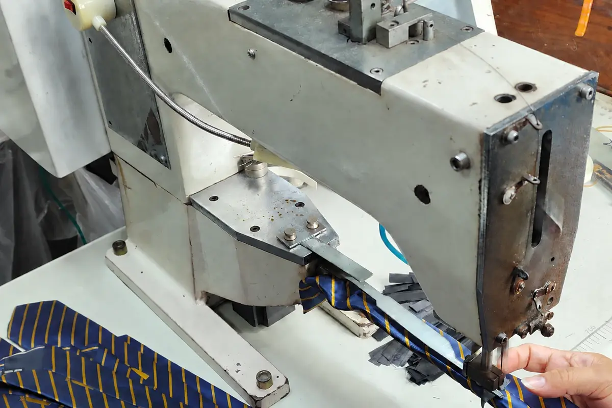 Hands guiding a blue and yellow striped tie through a sewing machine.