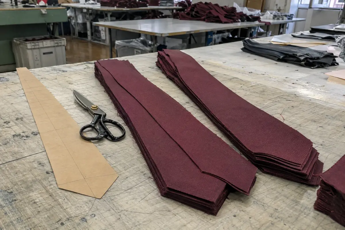 Stacks of cut necktie fabric panels beside a paper pattern and tailor shears.