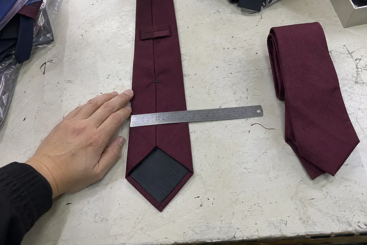 A ruler placed across a burgundy necktie during a width check.