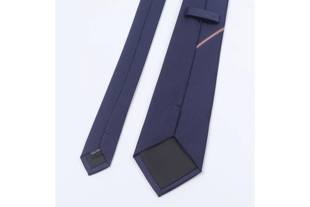 Navy tie reverse with a small label, keeper loop, center seam and dark tipping.