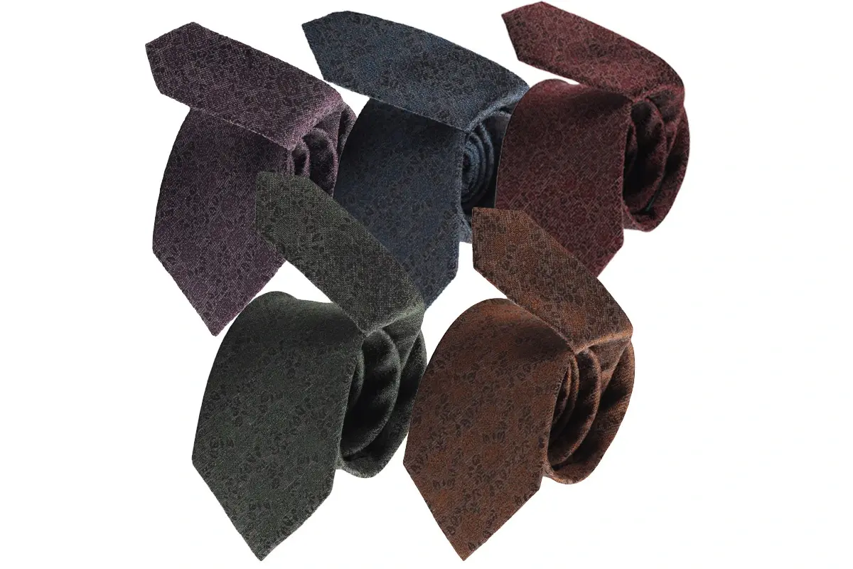 Six rolled ties in muted green, blue, brown and burgundy with textured surfaces.