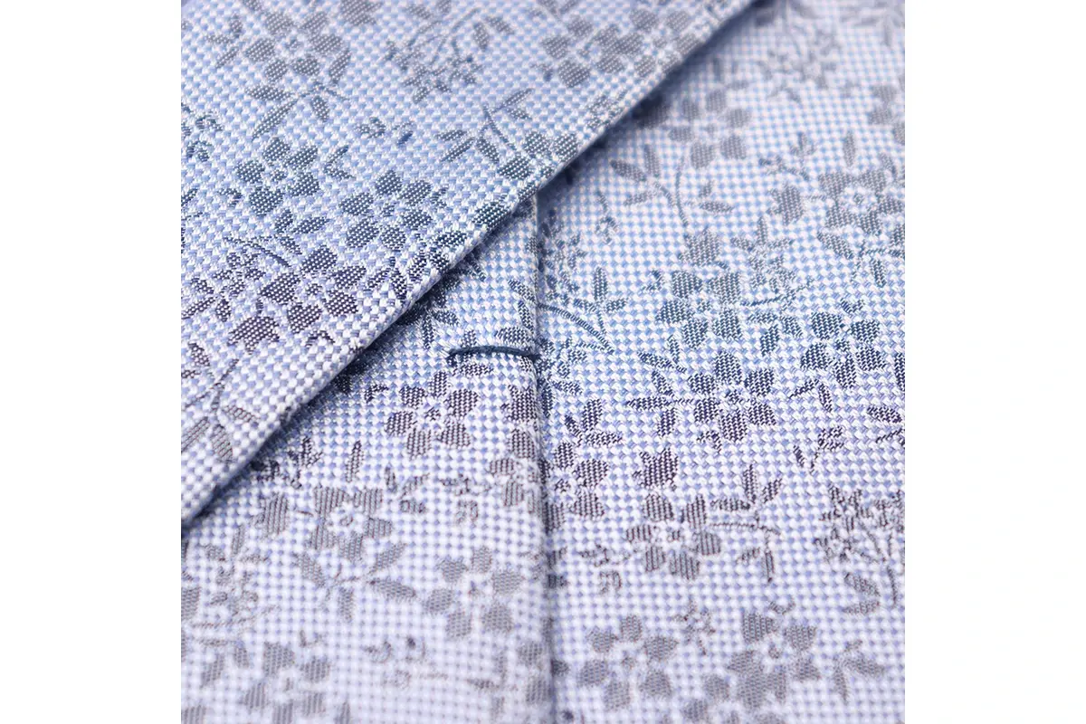Pale jacquard fabric with small grey floral motifs and visible yarn texture.