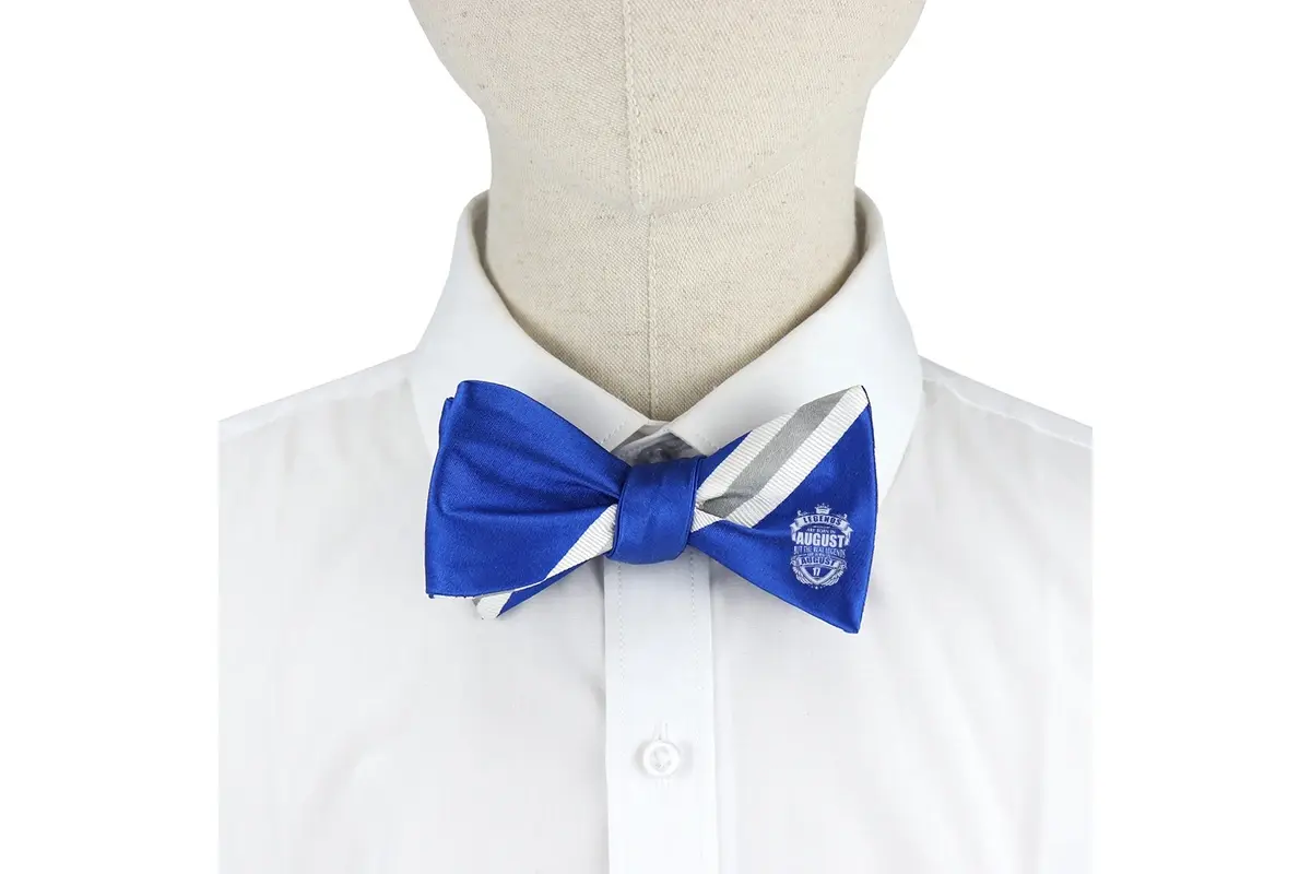 Blue and white bow tie worn on a white shirt with a crest visible on one wing.