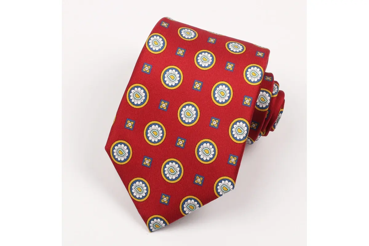 Rolled red tie with repeating circular emblems in yellow, blue and white.