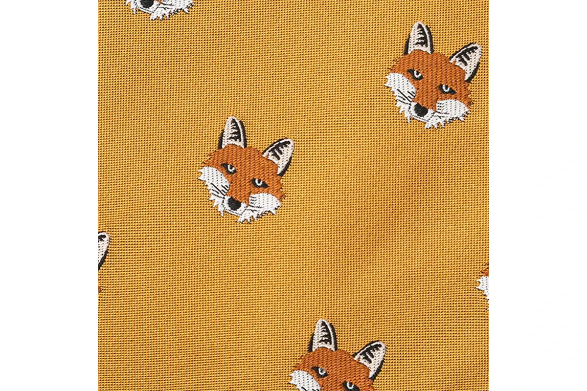 Close-up of small fox motifs spaced across a mustard-colored fabric surface.