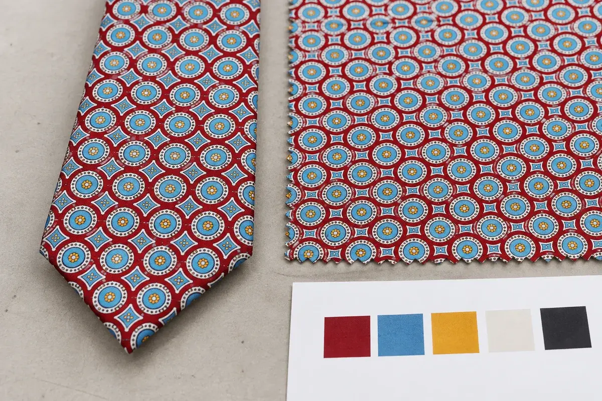 Finished red patterned tie beside coordinated printed fabric and color approval.
