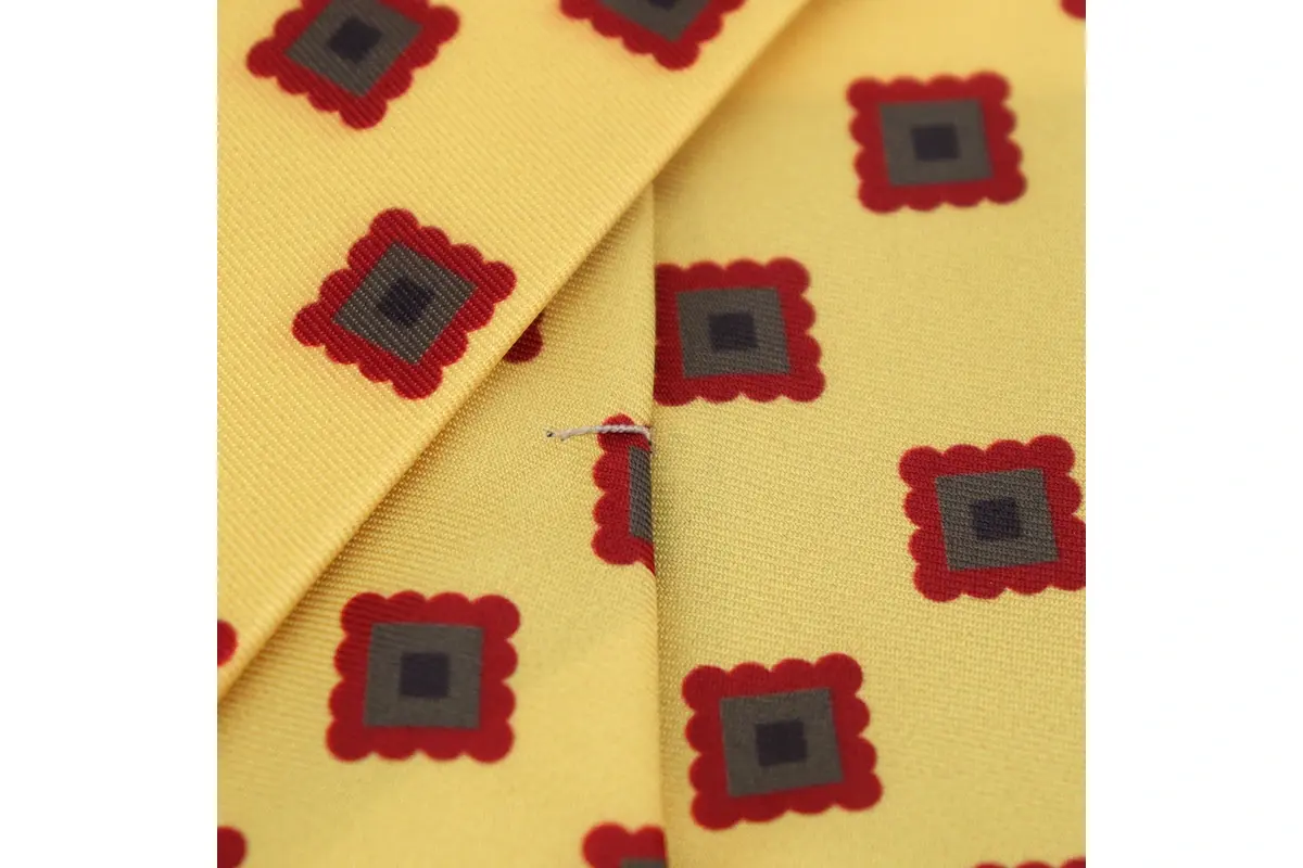 Red and dark square motifs printed on yellow fabric, showing color edges.