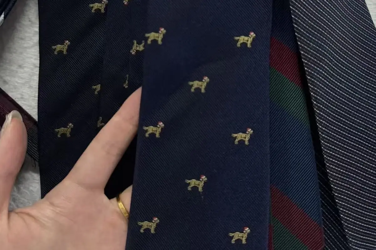 Hand holding a navy tie sample with small gold animal motifs.