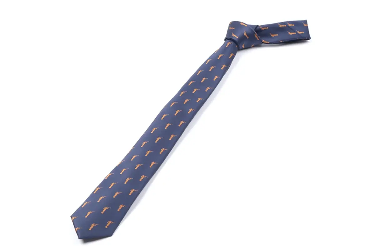 Knotted navy tie with tapered blade, narrow tail and small repeated motifs.
