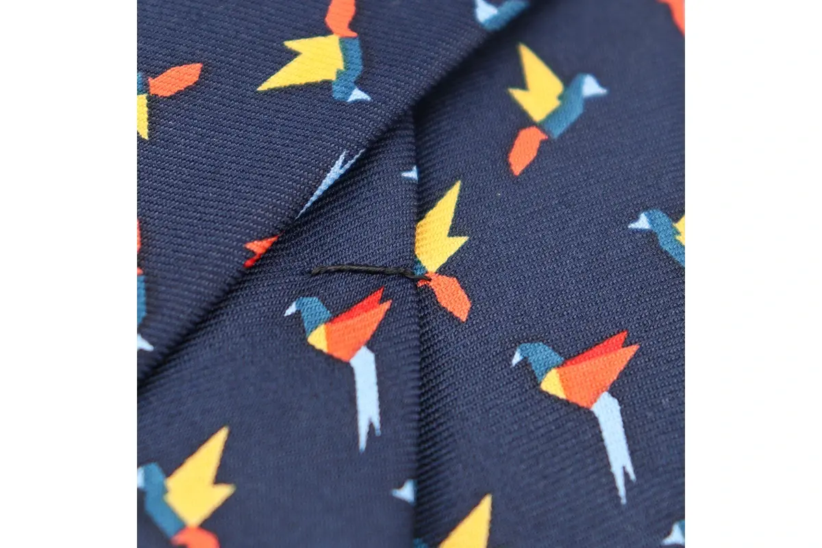 Close-up of multicolor angular bird illustrations on a navy tie surface.