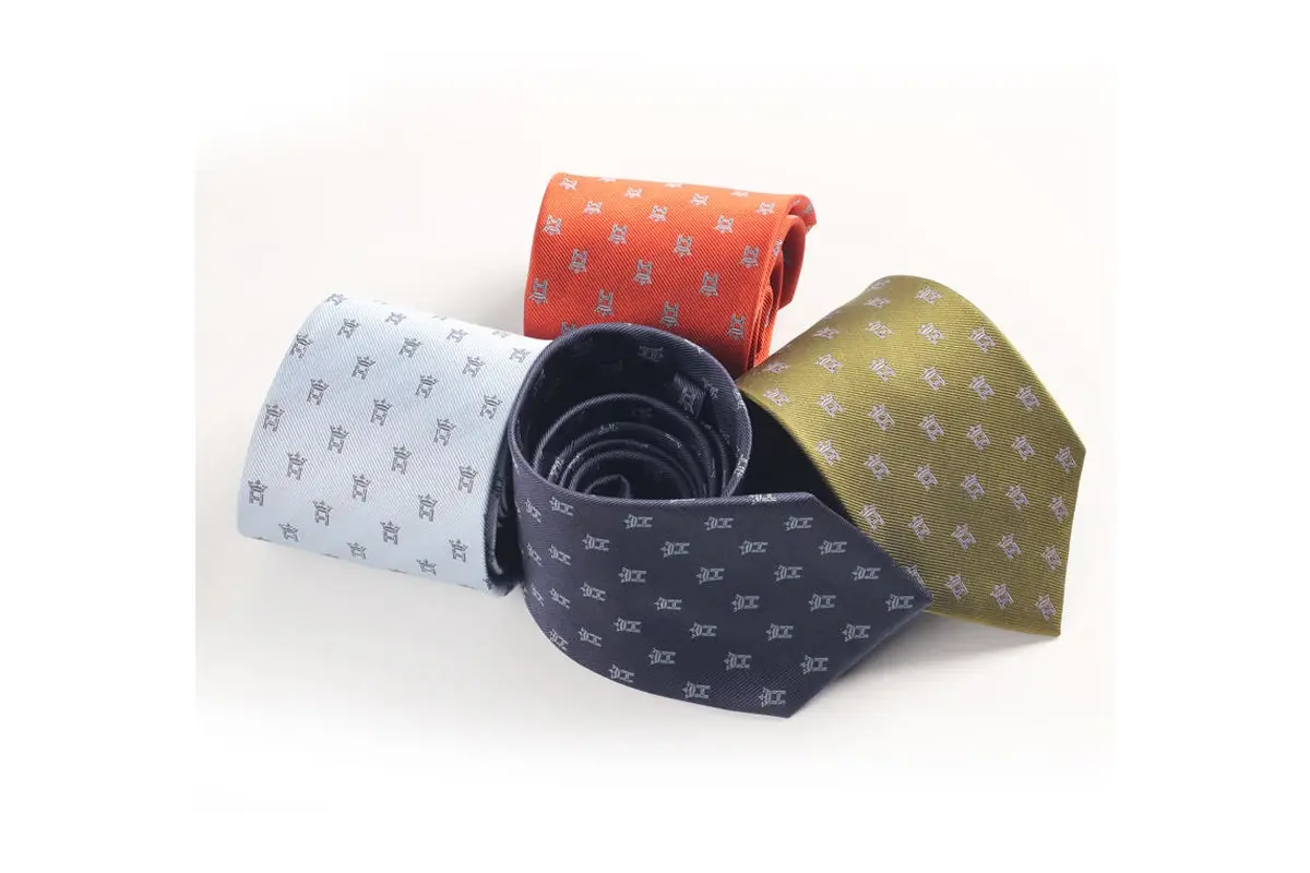 Four rolled ties in pale blue, orange, navy and olive with small motifs.