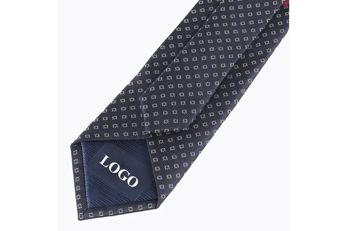 Dark geometric tie reverse with a center seam and sample mark on tipping.
